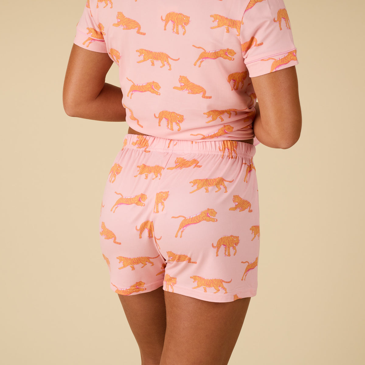 Person wearing a pink pajama set with orange tiger patterns on a beige background