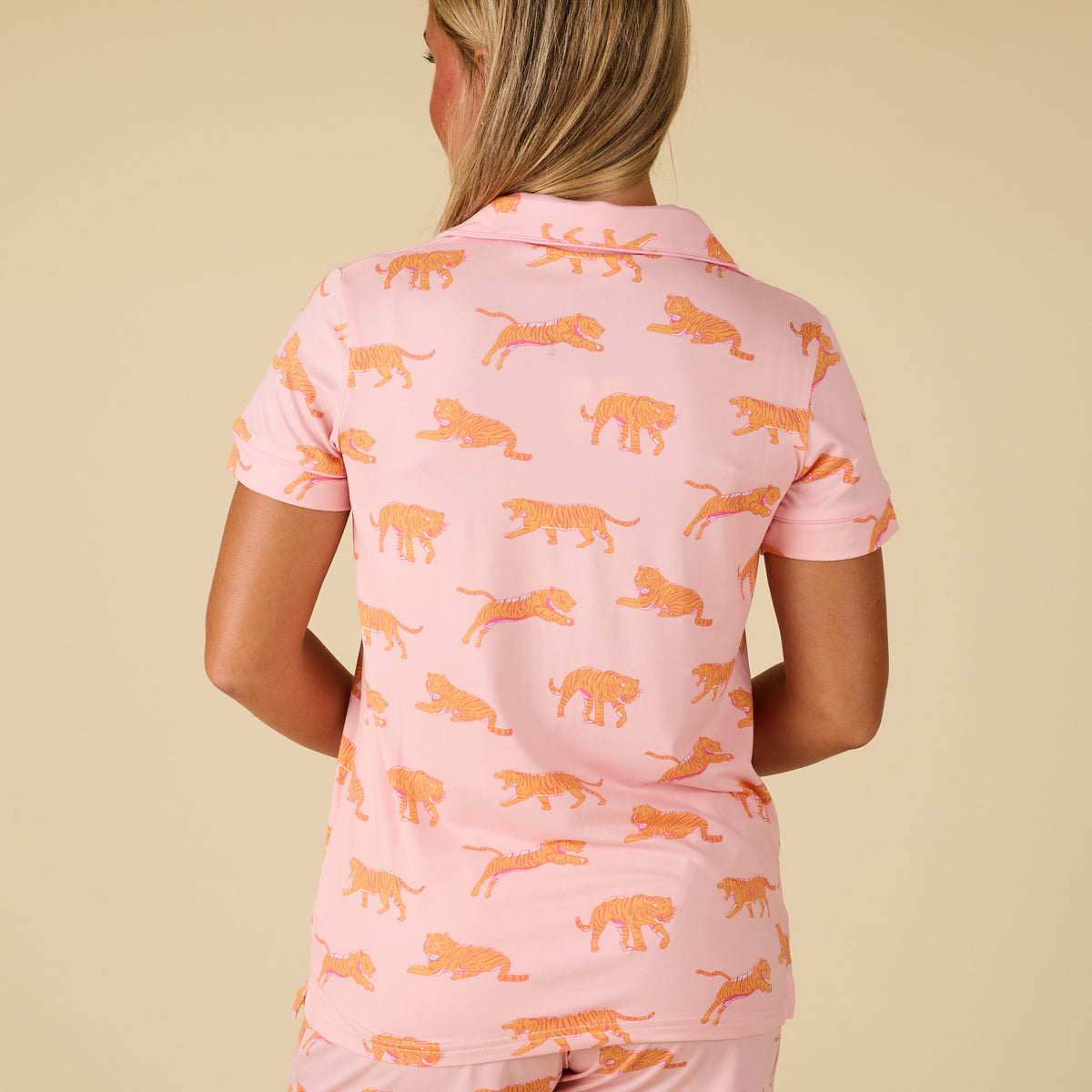 Person wearing a pink pajama set with orange tiger patterns on a beige background