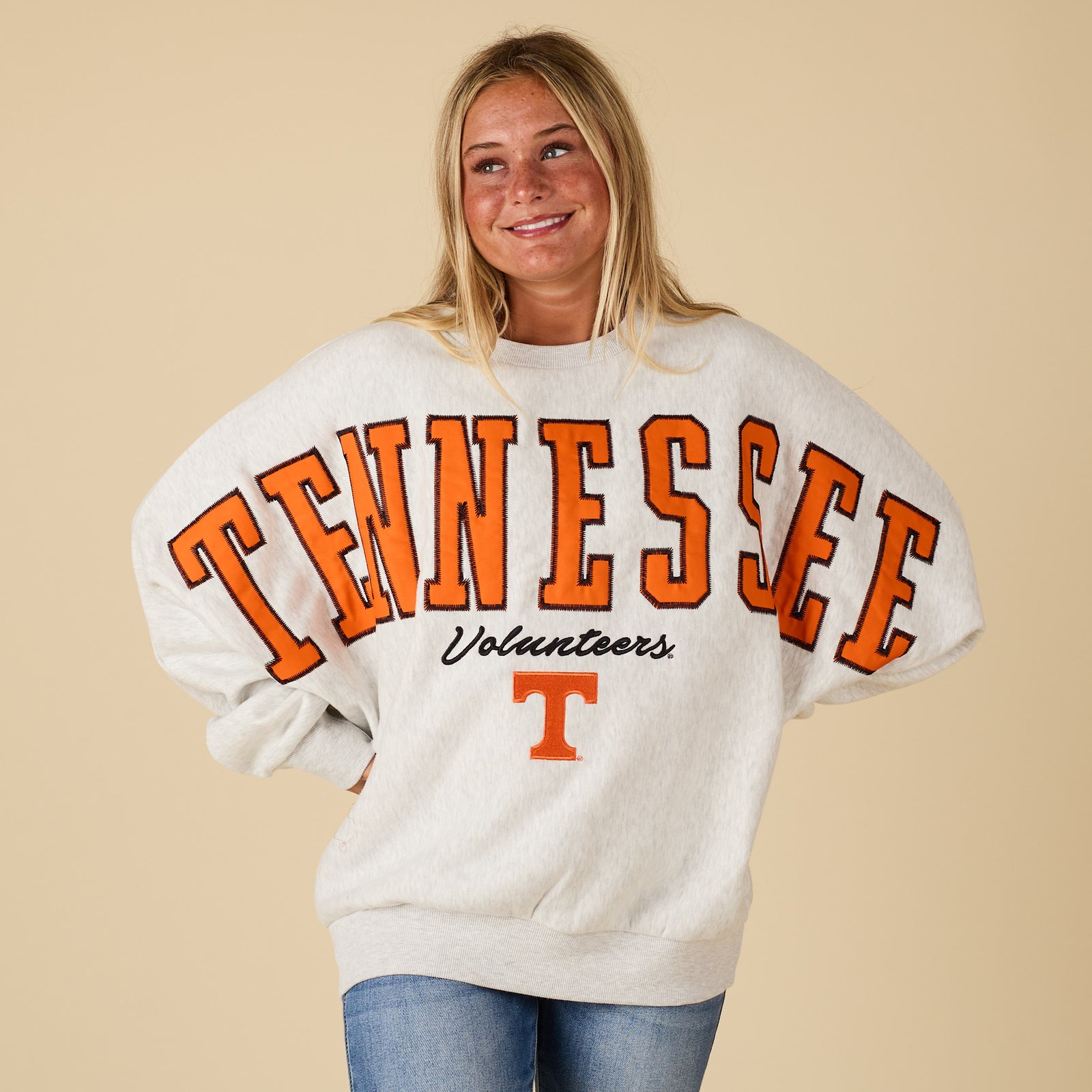 Person wearing a 'Tennessee Volunteers' sweatshirt on a beige background