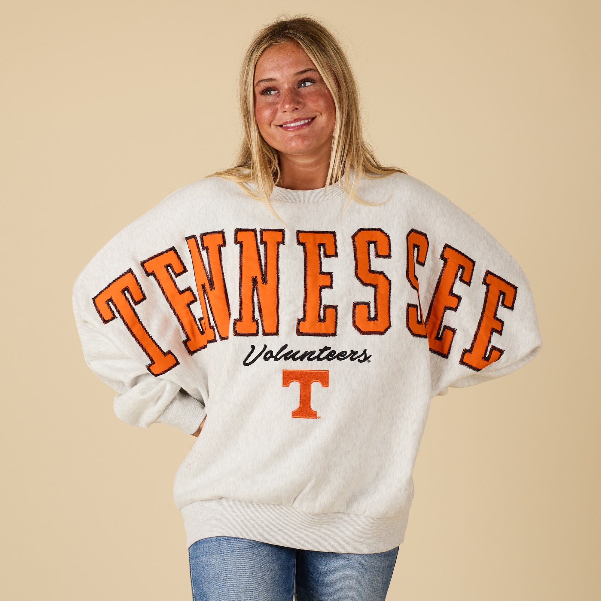 Person wearing a 'Tennessee Volunteers' sweatshirt on a beige background