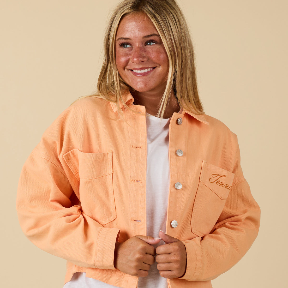 Front view of orange cropped jacket with Tennessee embroidery on chest pocket, styled on model with white tee and jeans.