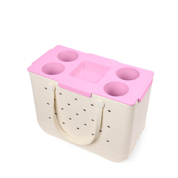 Pink plastic tray with multiple openings on top of a beige Bogg Bag shown on a white background.