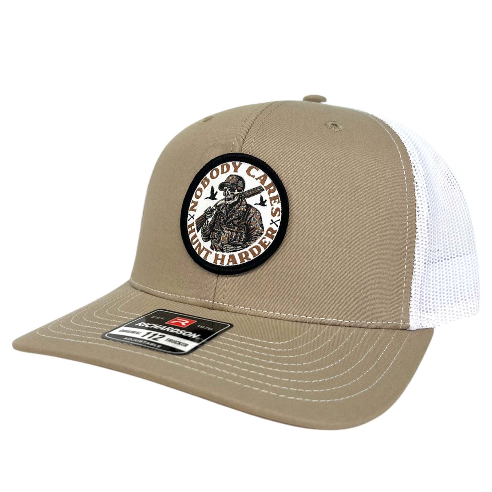 Good Ole Boys Adjustable Trucker Hat, color khaki and white. This hat features a patch sewn on the front with a skeleton wearing camouflage hunting gear and the words "Nobody cares, Hunt Harder" around the design. Adjustable snapback closure, soft mesh backing, mid-profile, pre-curved PE visor.