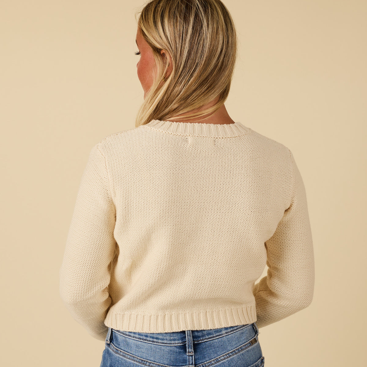 Back view of ivory cropped cardigan sweater with ribbed hem and long sleeves.