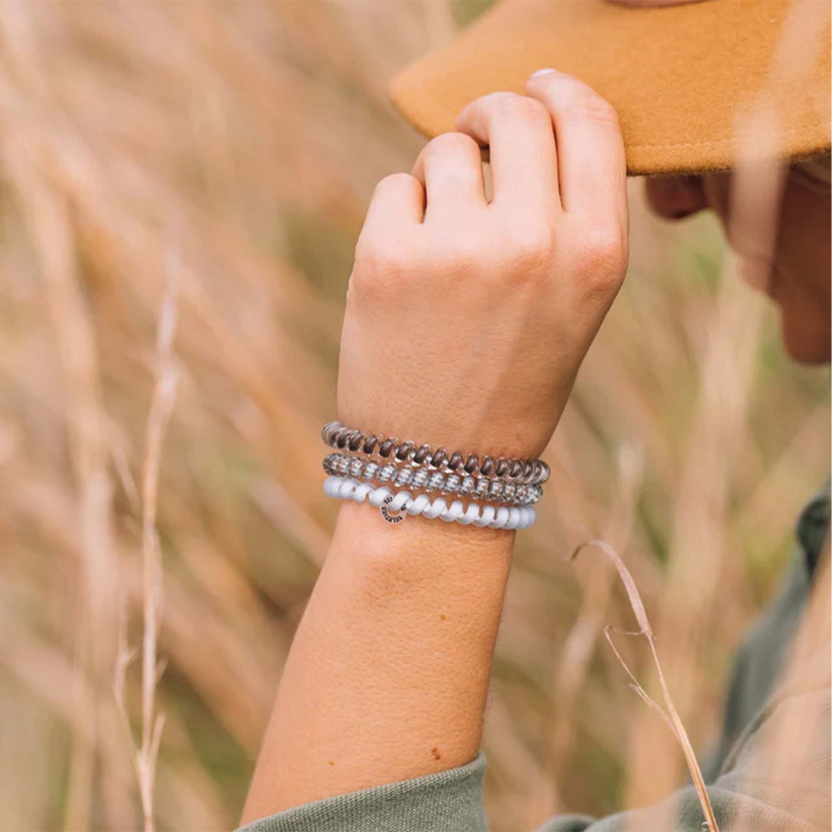 Teleties Small Hair Ties 3-Pack in Truly Taupe styled on wrist with metallic brown, taupe diamond, and light blue bands stacked.