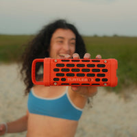 Woman holding up a Turtlebox Ranger speaker to the camera.