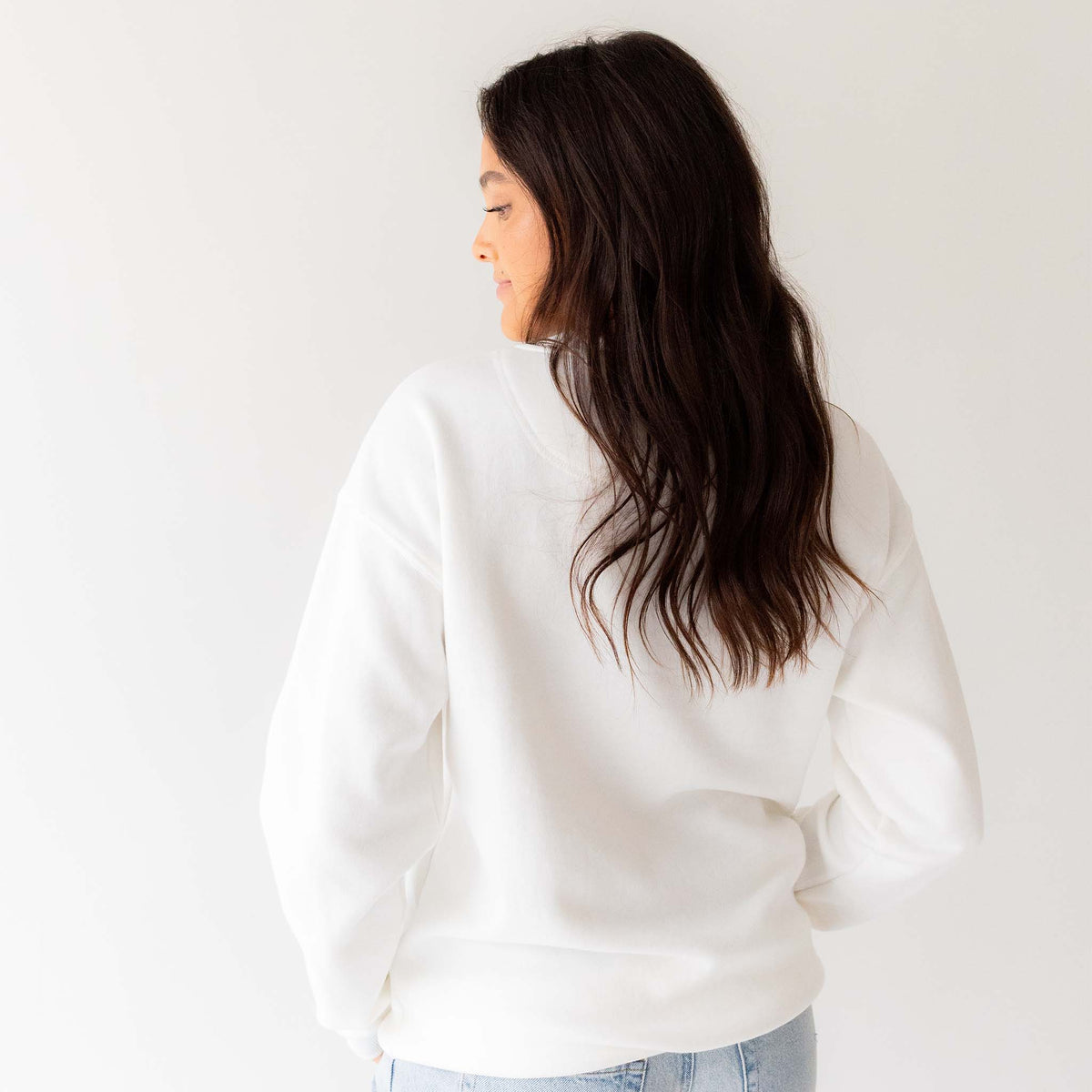 Woman wearing plain white University of Georgia crewneck sweatshirt with no design, paired with light-wash jeans.