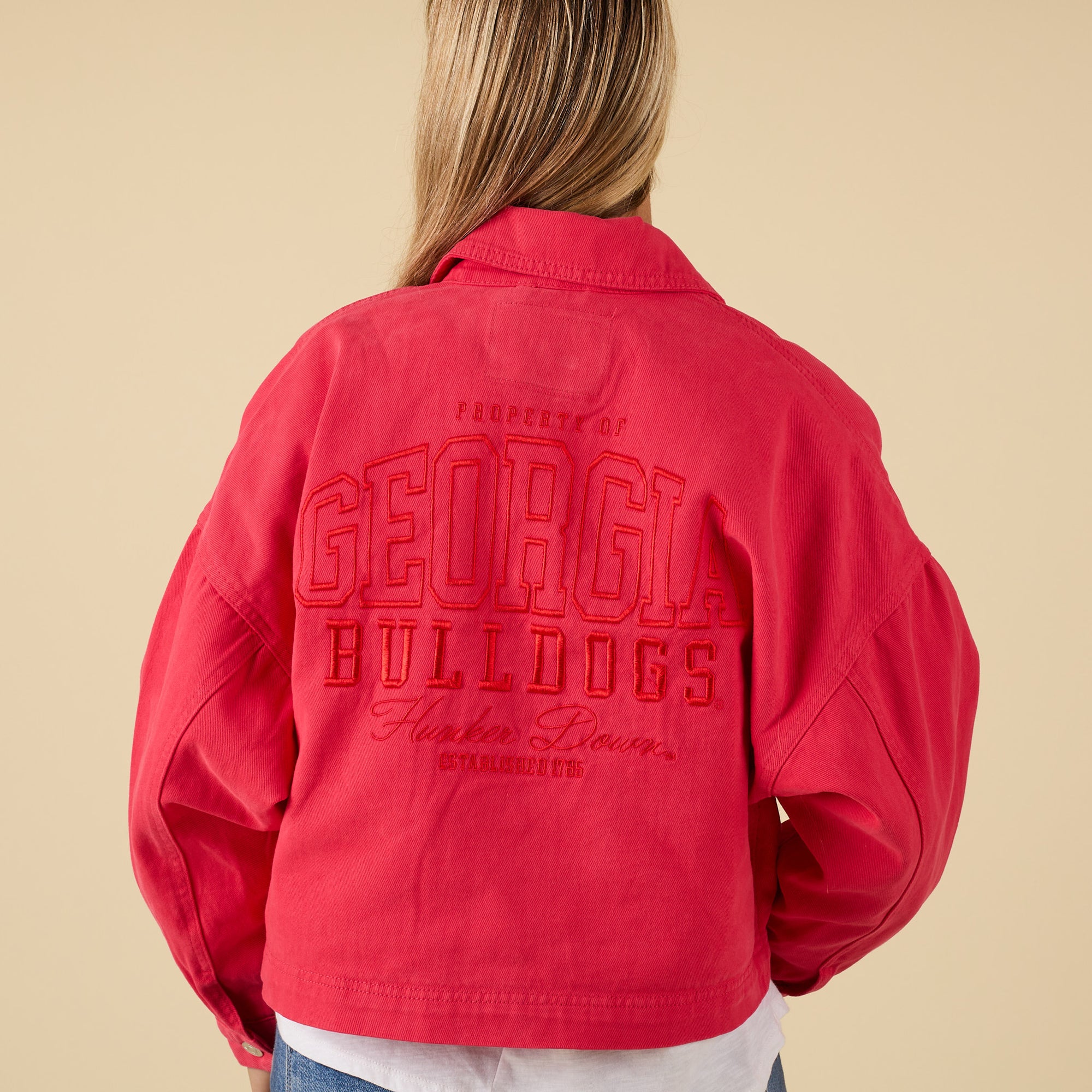 Red jacket with 'Georgia Bulldogs' embroidered text on the back against a beige background