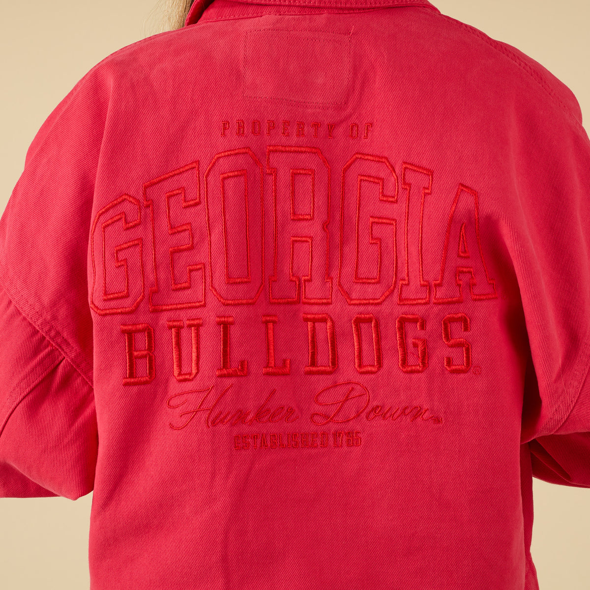 Red jacket with 'Georgia Bulldogs' embroidered text on the back against a beige background