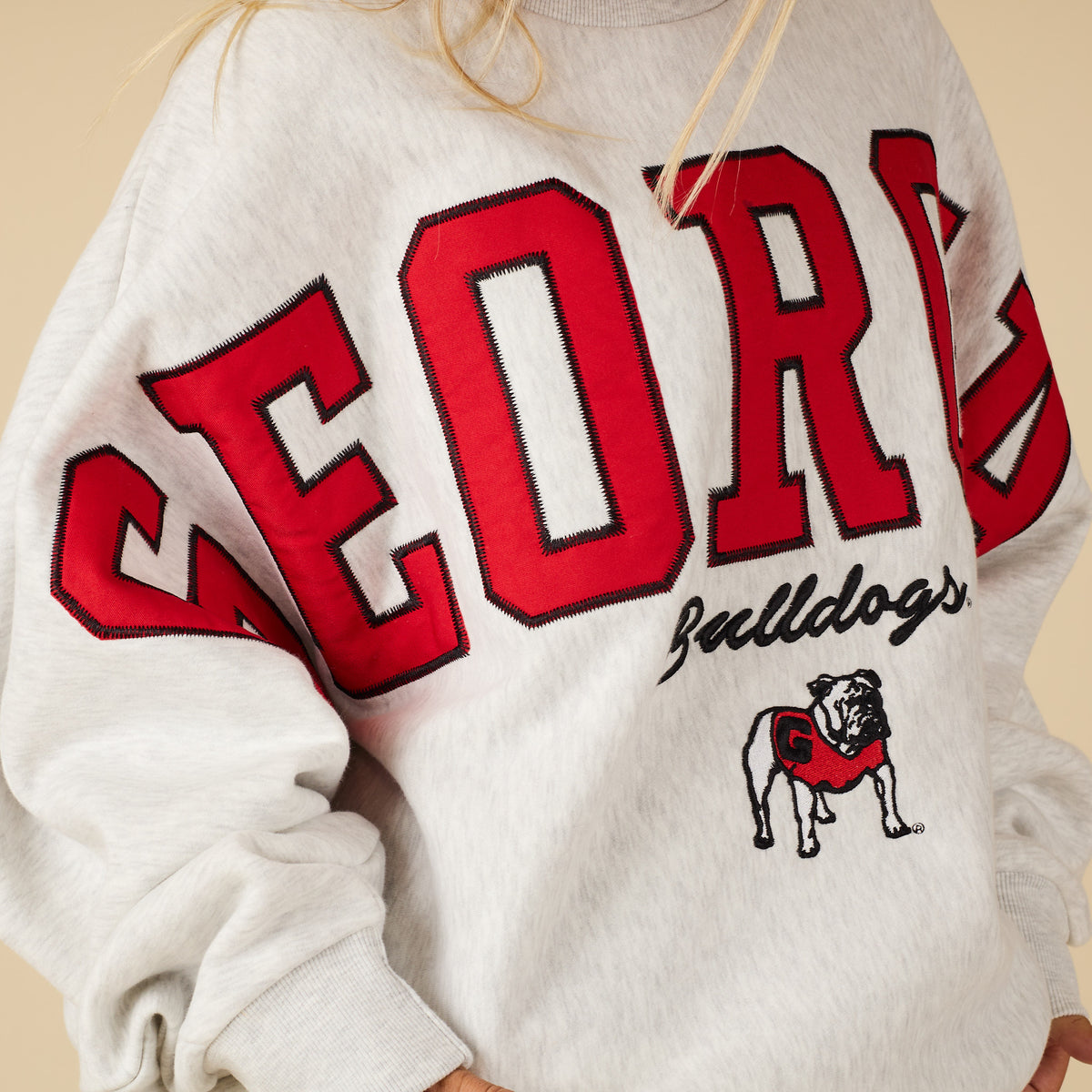 White sweatshirt with red and black text and bulldog logo on a beige background