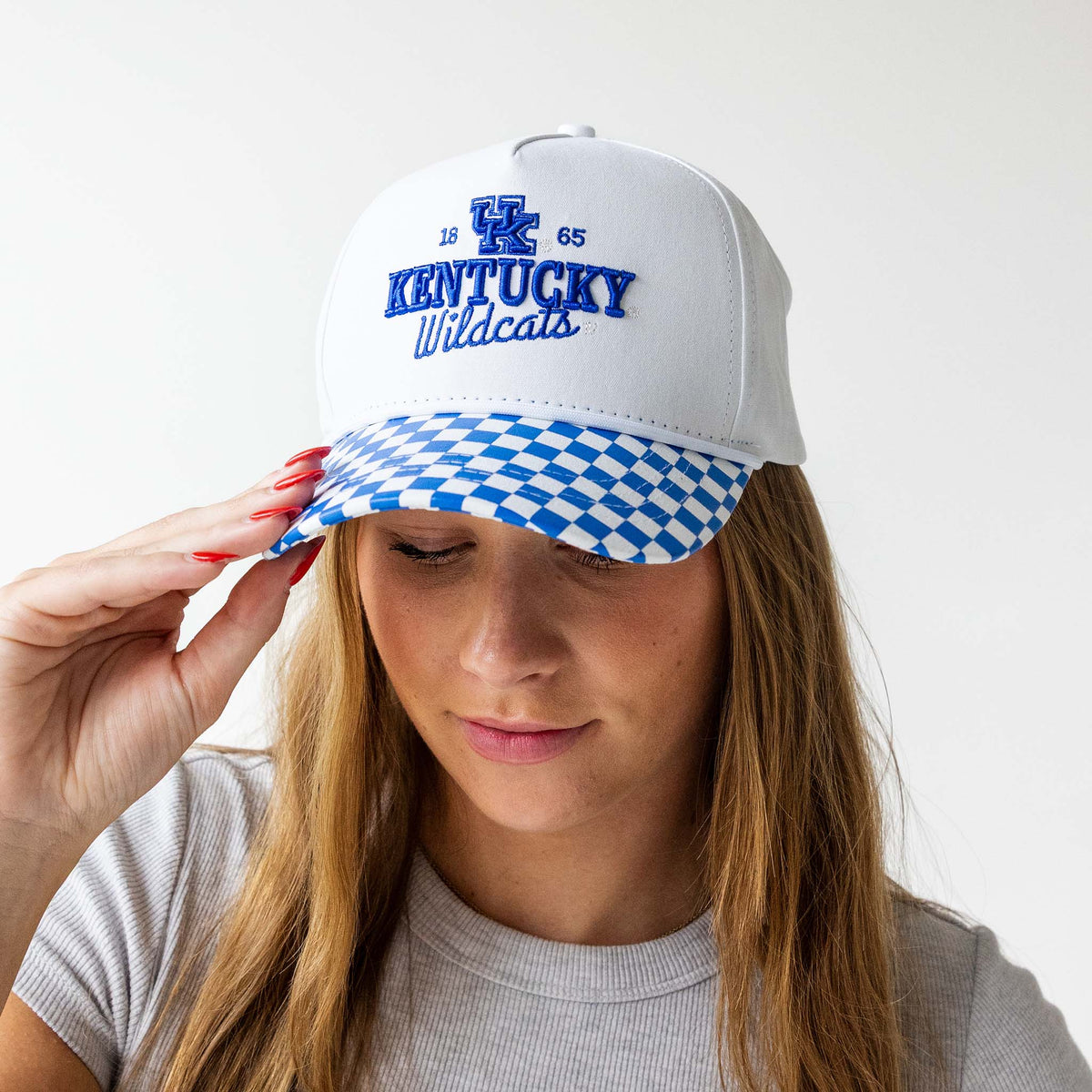 Kentucky Wildcats white cap with embroidered logo and blue checkered brim, worn by a model facing forward adjusting the bill.