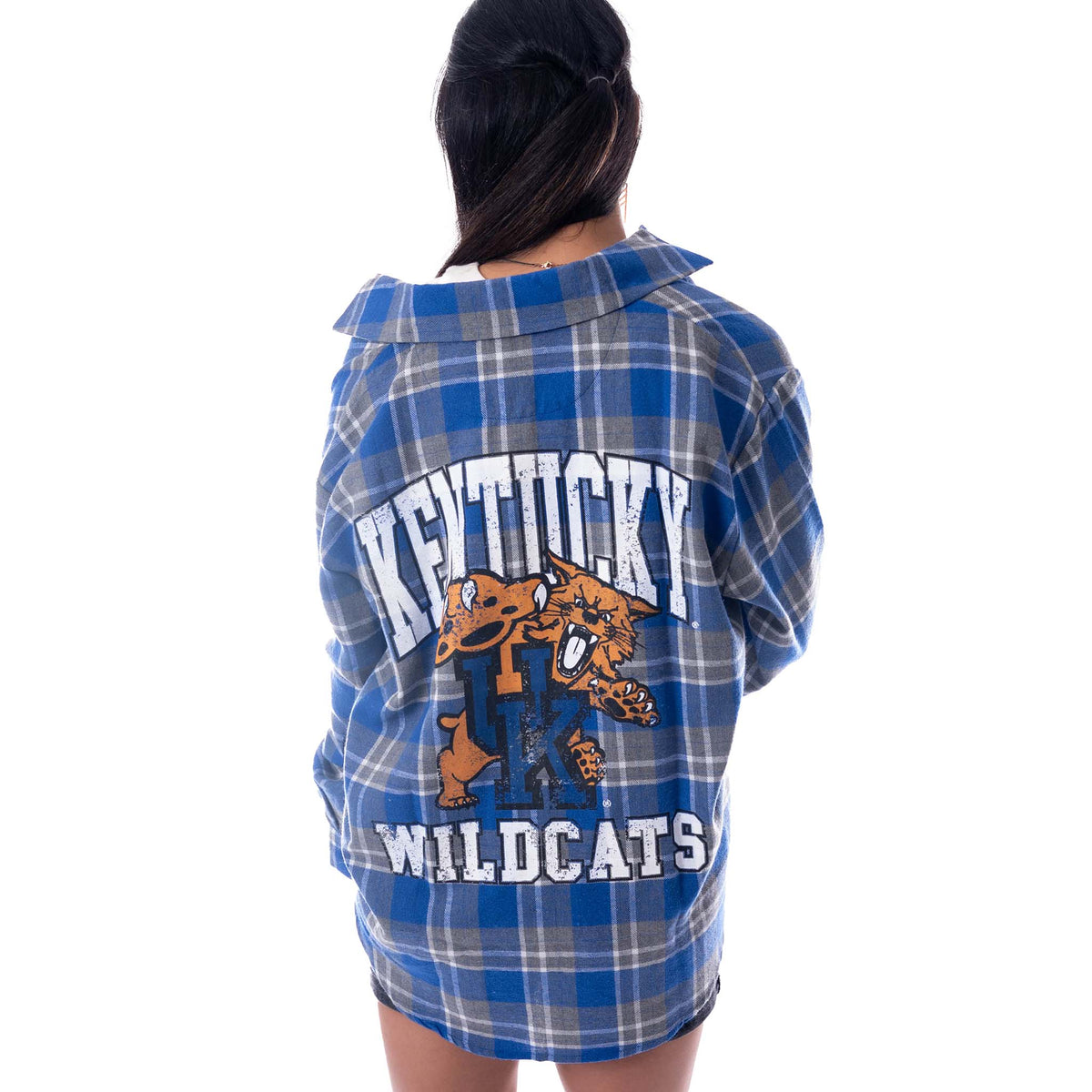 Back view of a woman wearing a blue and grey plaid Kentucky Wildcats flannel shirt with large white “Kentucky Wildcats” text and wildcat mascot graphic.