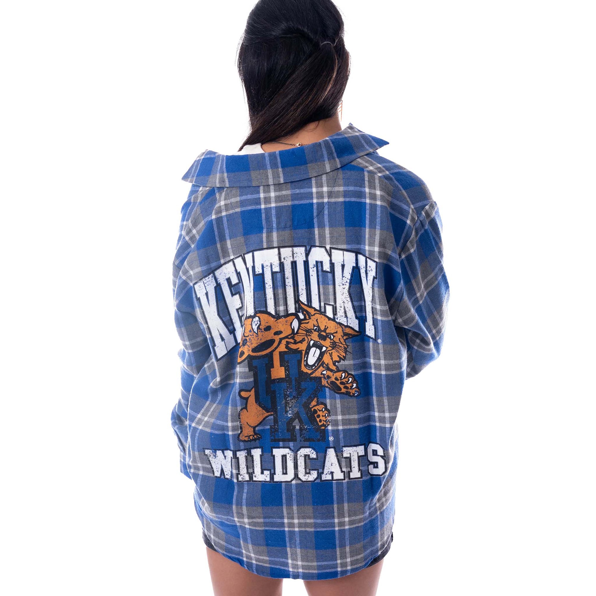 Back view of a woman wearing a blue and grey plaid Kentucky Wildcats flannel shirt with large white “Kentucky Wildcats” text and wildcat mascot graphic.