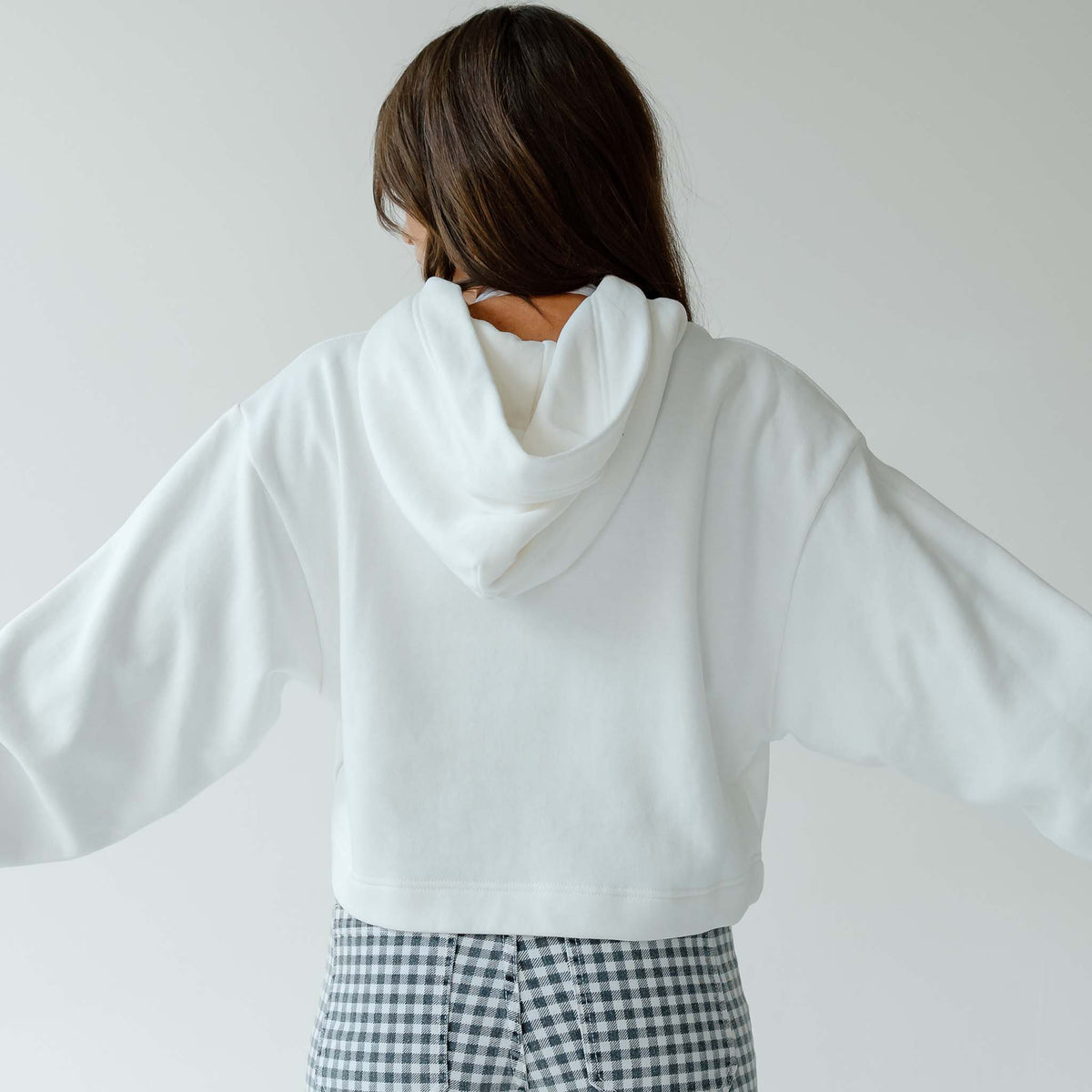Back view of woman wearing a plain white cropped hoodie with hood up, paired with gingham pants.