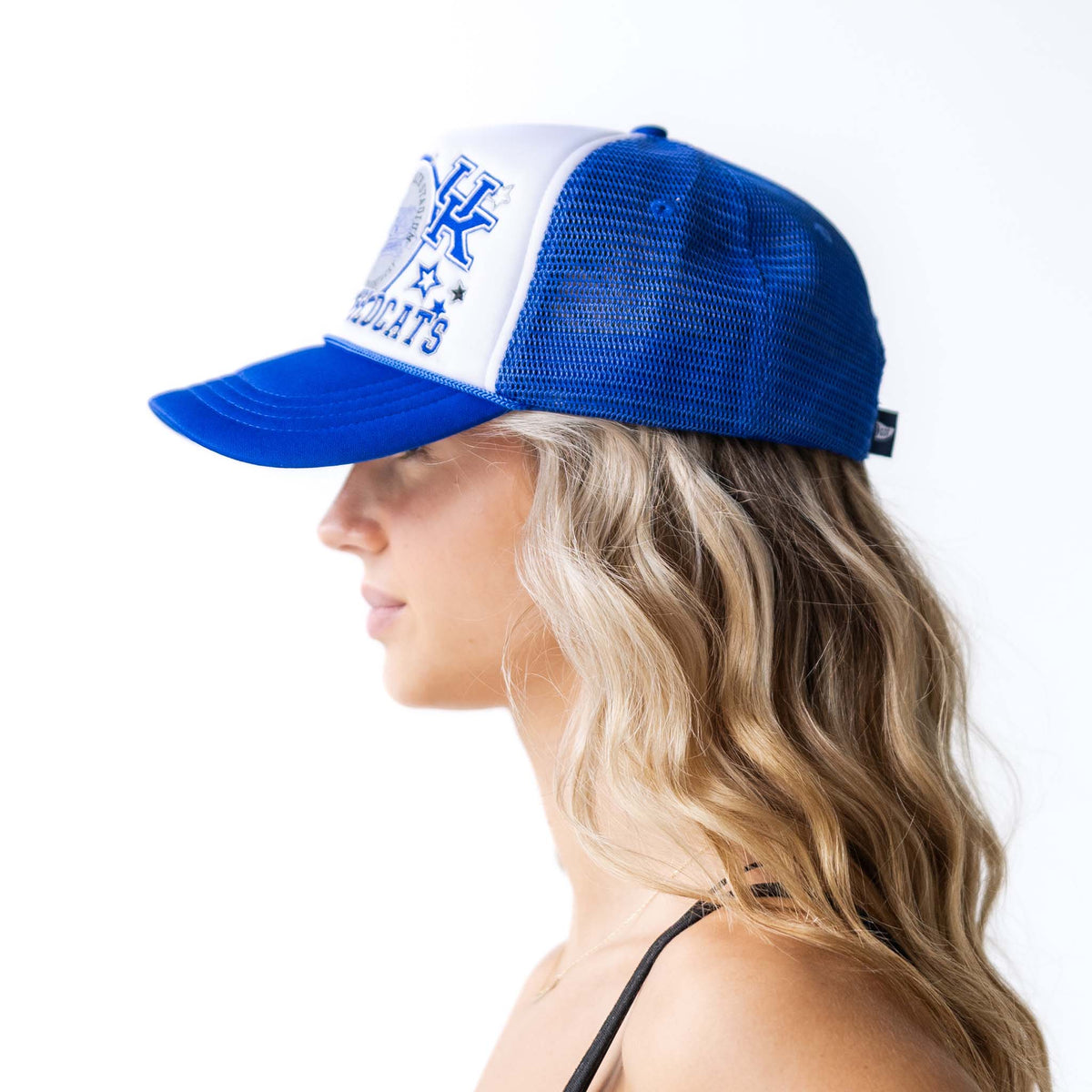 Side view of woman wearing a royal blue and white Kentucky Wildcats trucker hat with mesh back and curved brim.