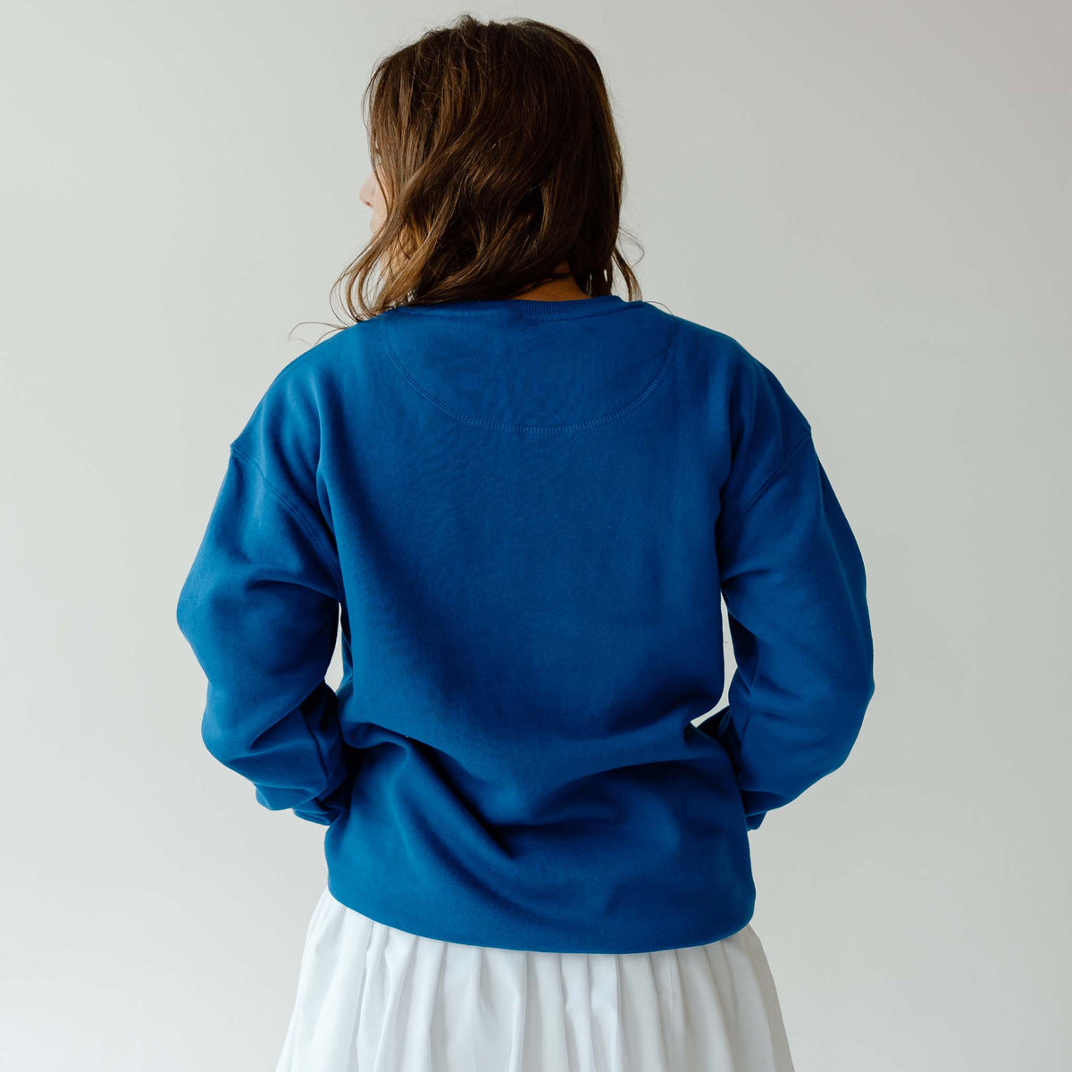 Back view of woman wearing plain royal blue crewneck sweatshirt with ribbed hem and cuffs.