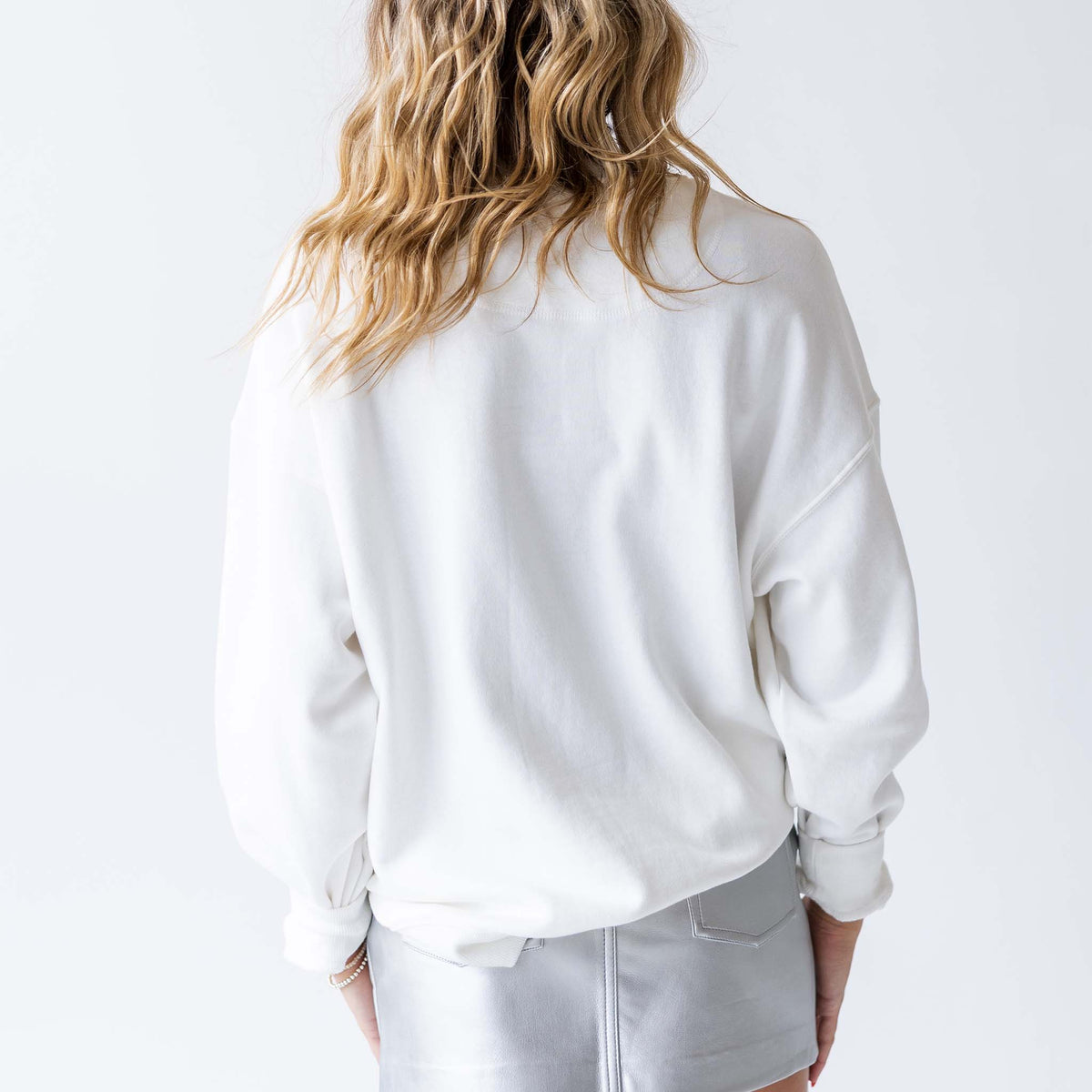 Back view of woman wearing plain white crewneck sweatshirt with ribbed hem and cuffs.