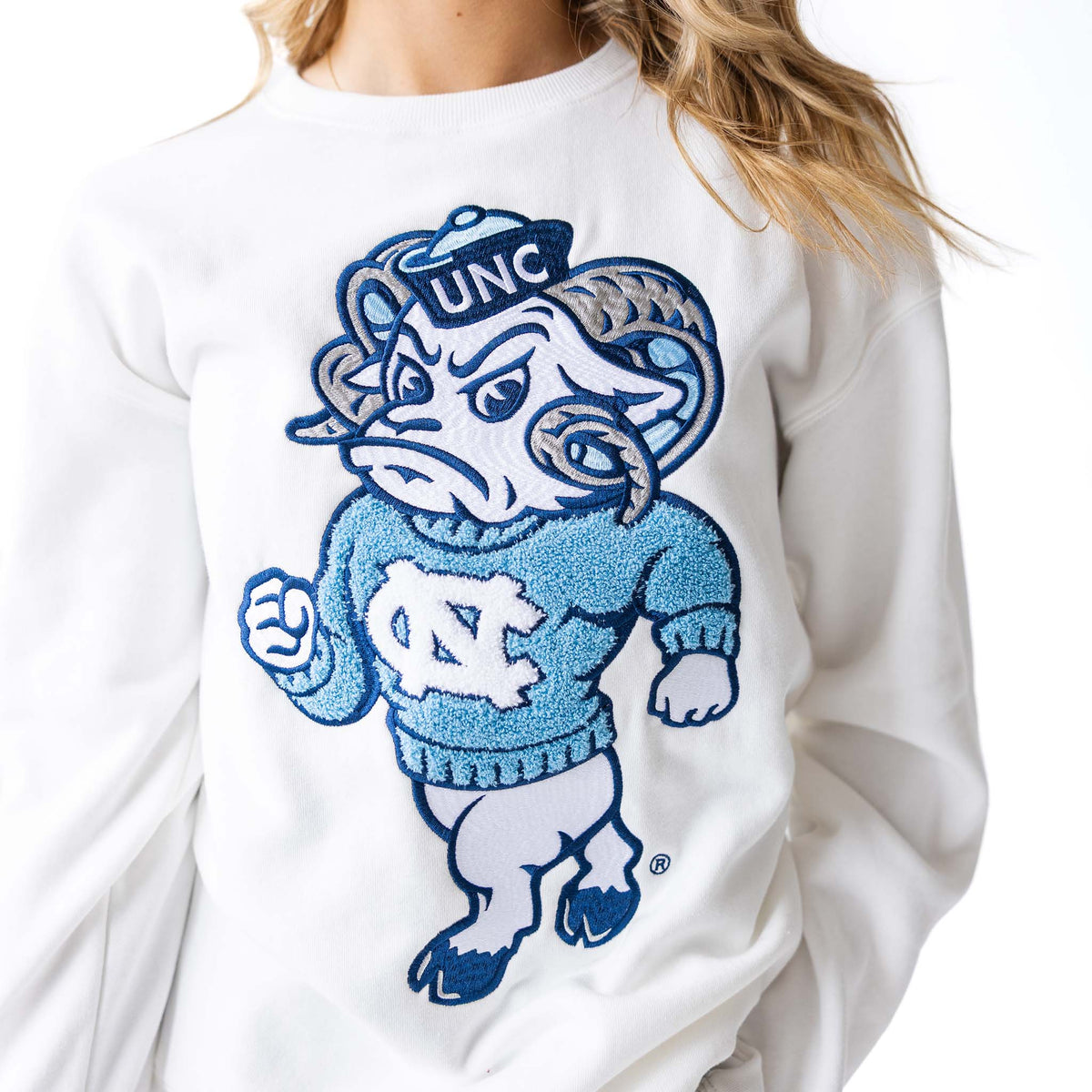 Close-up of white crewneck sweatshirt with oversized chenille UNC Rameses mascot patch.