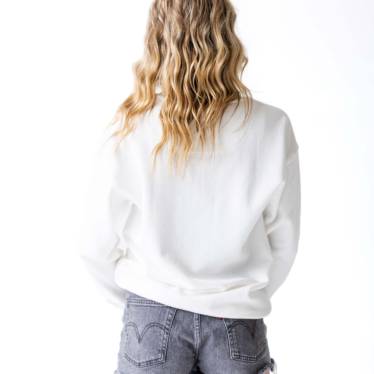 Back view of woman wearing plain white crewneck sweatshirt with ribbed hem and cuffs.