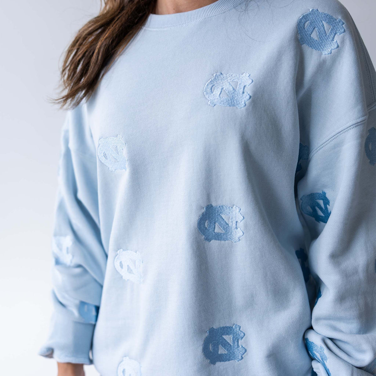 Close-up of light blue crewneck sweatshirt with allover tonal embroidered UNC logos.