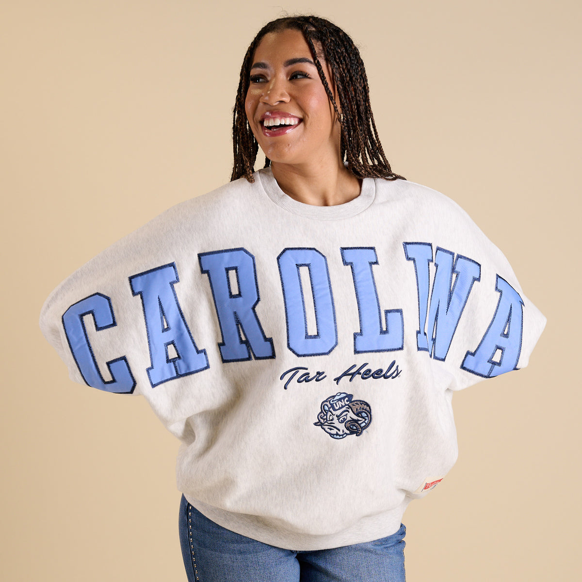 Model wearing oversized ash gray UNC crewneck with large Carolina blue lettering and Tar Heels mascot.