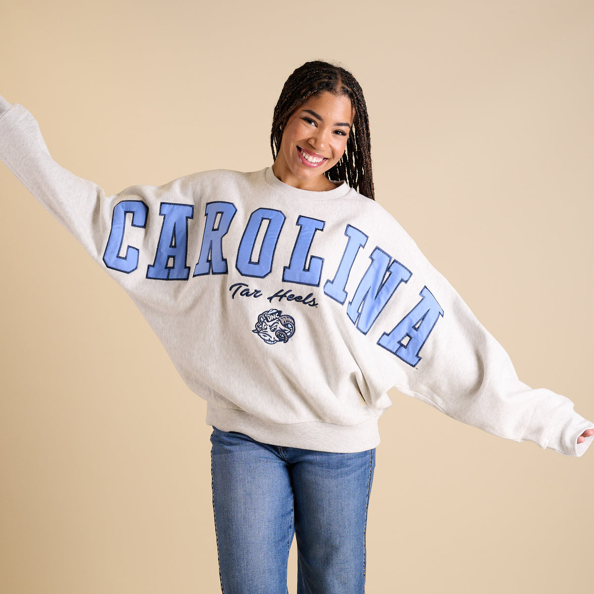 Model wearing oversized ash gray UNC crewneck with large Carolina blue lettering and Tar Heels mascot.