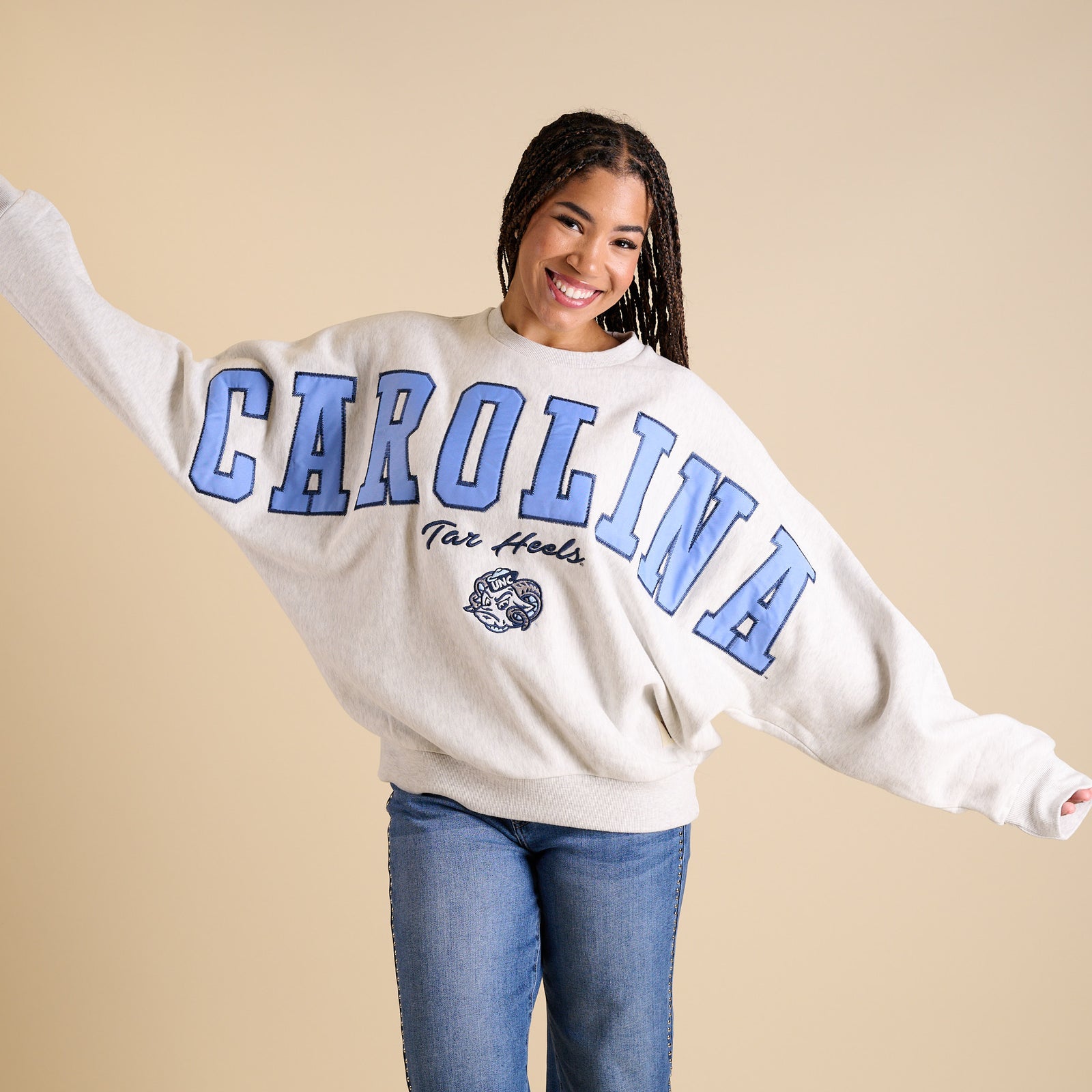 Model wearing oversized ash gray UNC crewneck with large Carolina blue lettering and Tar Heels mascot.