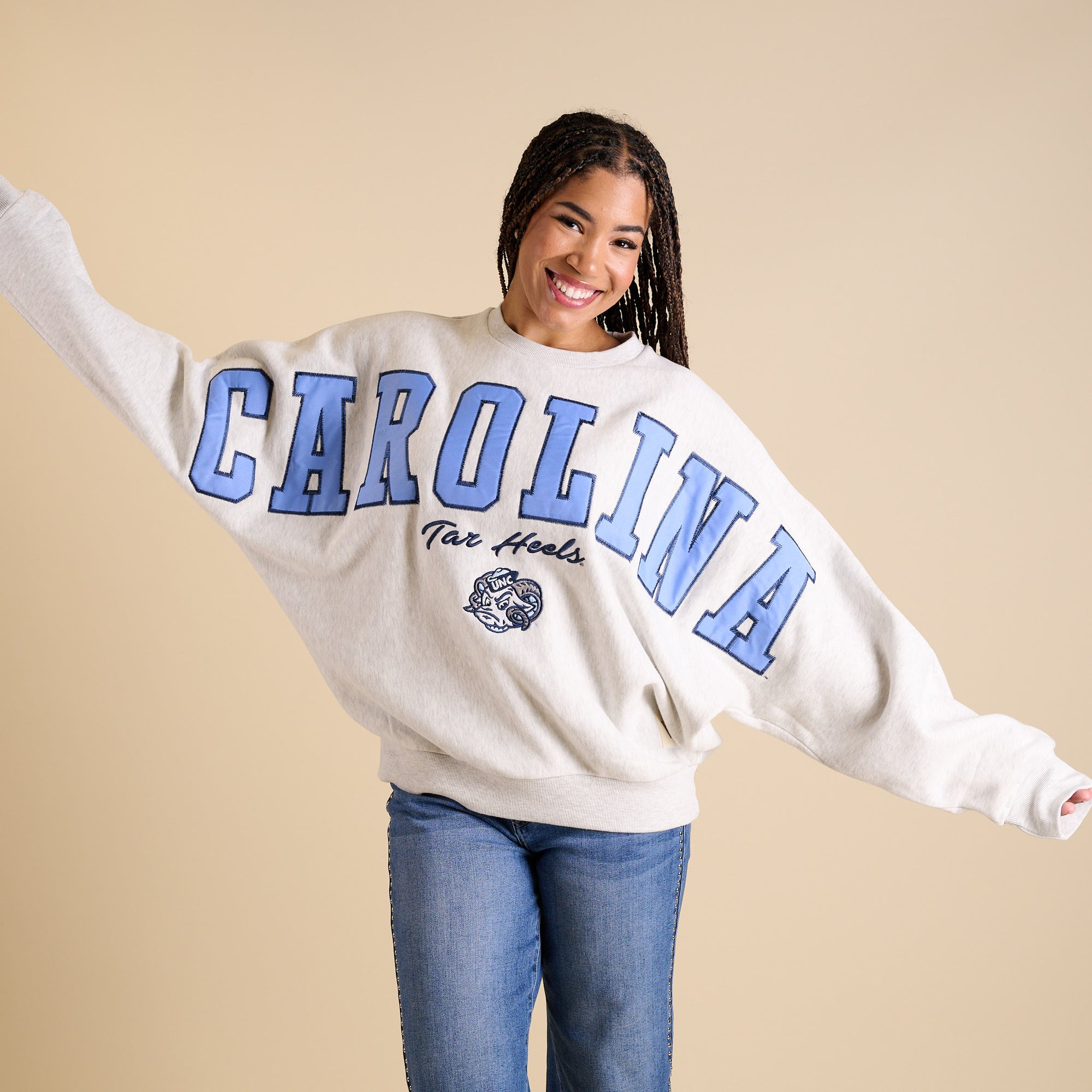 Model wearing oversized ash gray UNC crewneck with large Carolina blue lettering and Tar Heels mascot.