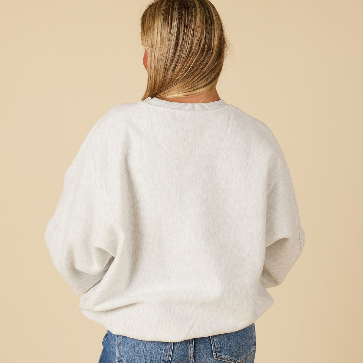 Person wearing a light gray sweater and blue jeans on a beige background
