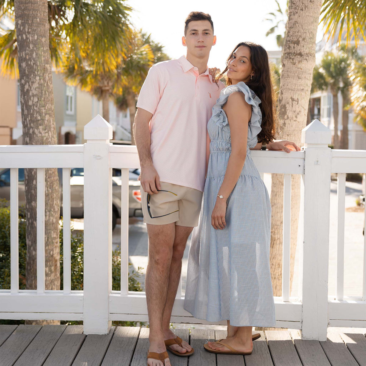 Sky| Two people standing on a wooden deck with palm trees in the background