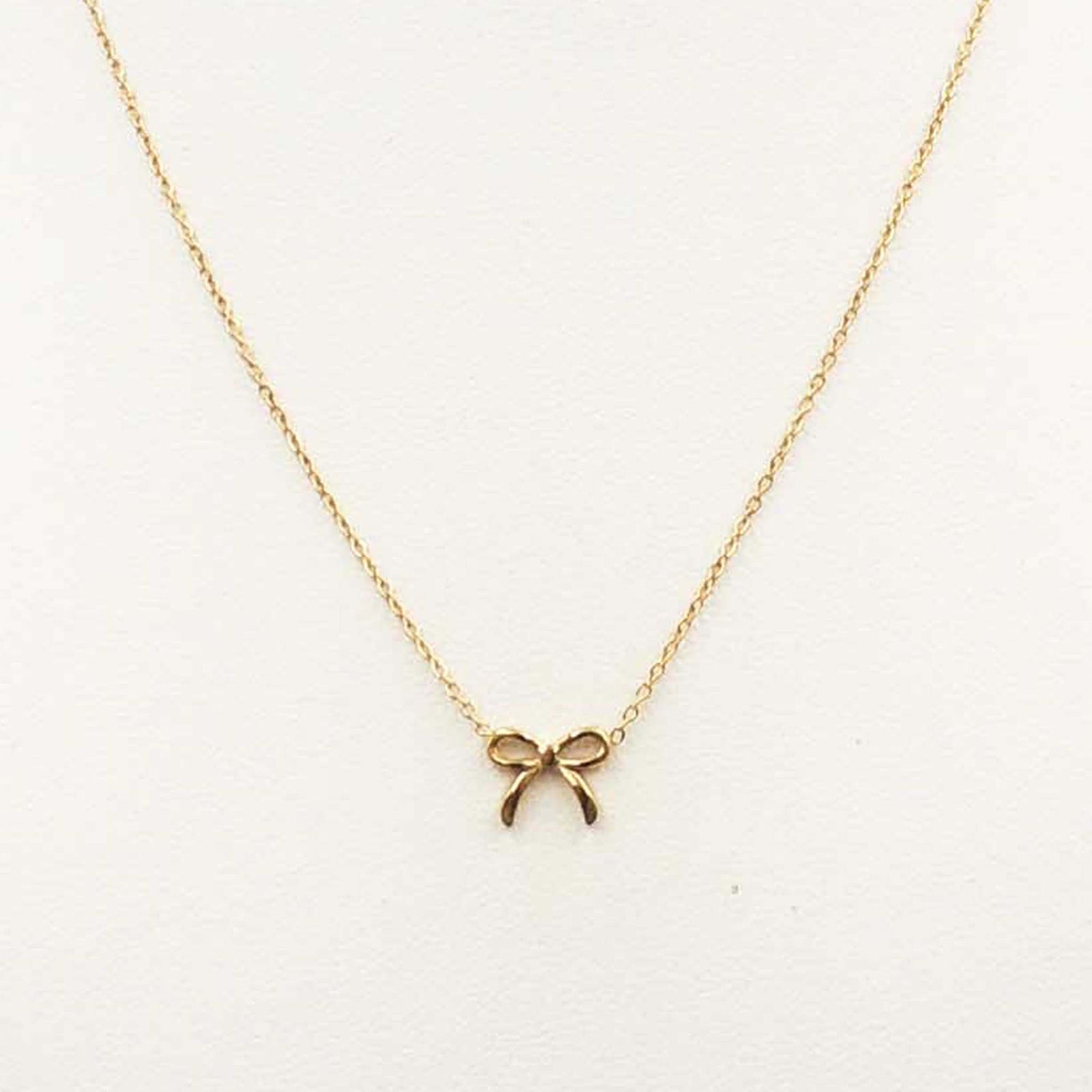 Fine gold chain necklace with a small bow-shaped pendant in the center, displayed on a light background.
