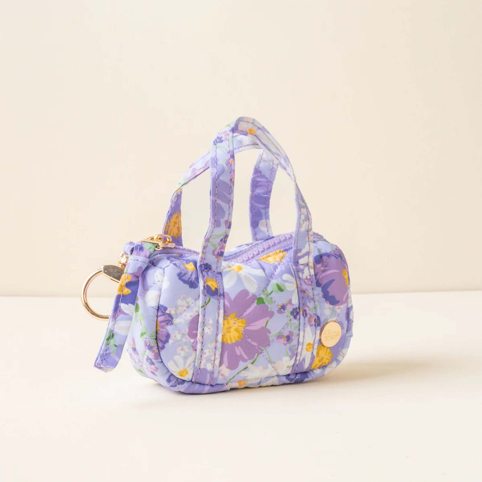 Side view of purple floral mini duffle keychain with top handles, gold keyring, and zip closure.