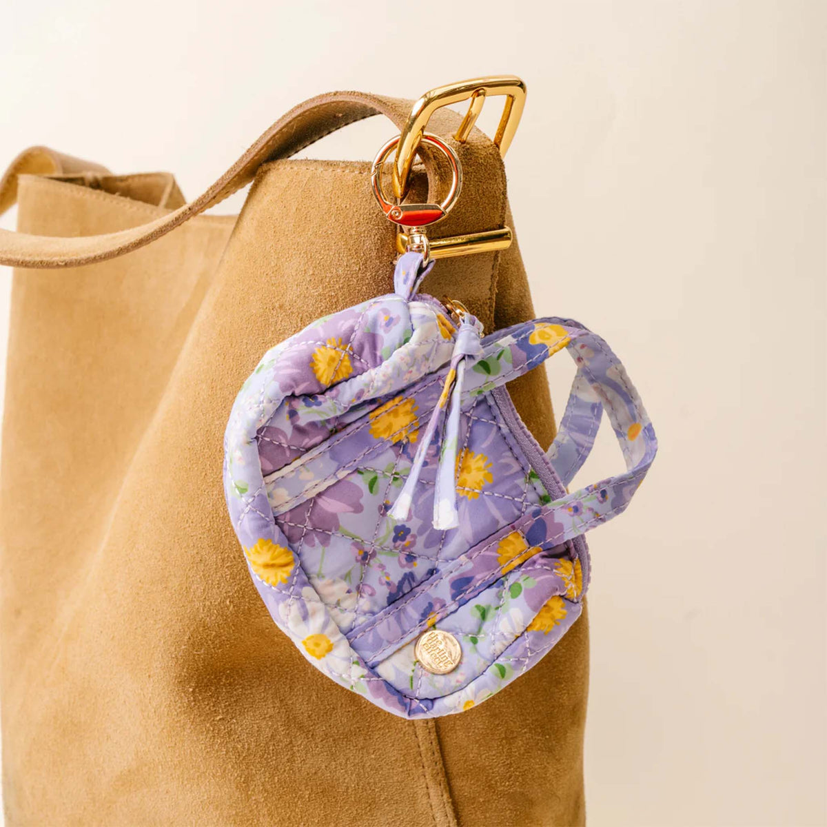 Purple floral mini duffle keychain clipped to a tan suede tote bag using the gold keyring.