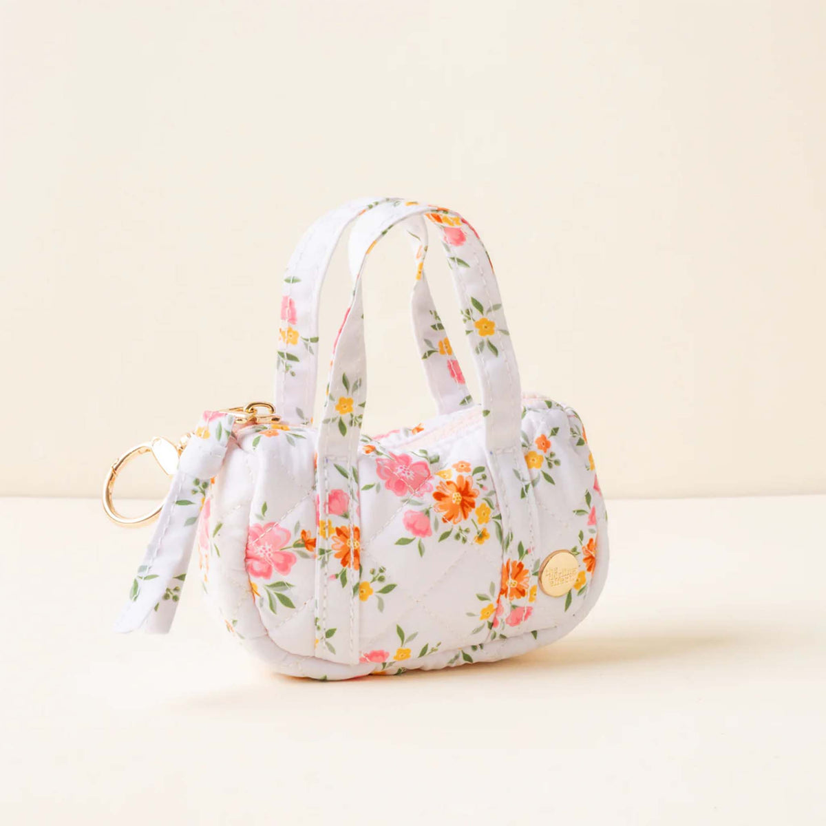 Side view of a white quilted mini duffle keychain bag with orange and pink floral print and gold hardware.