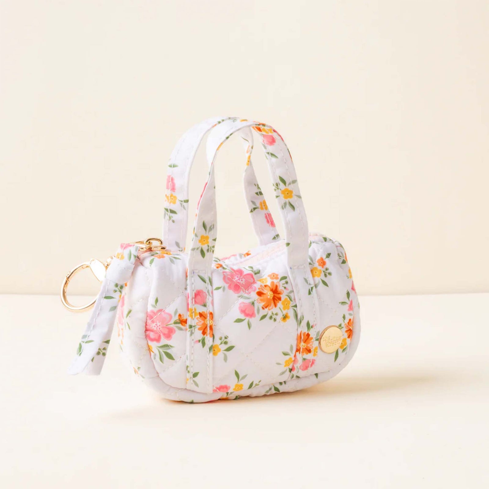 Side view of a white quilted mini duffle keychain bag with orange and pink floral print and gold hardware.