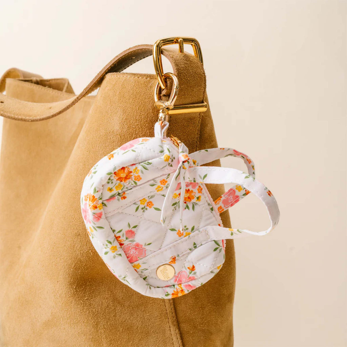 White floral mini duffle keychain clipped to a tan suede tote bag using the attached gold keyring.