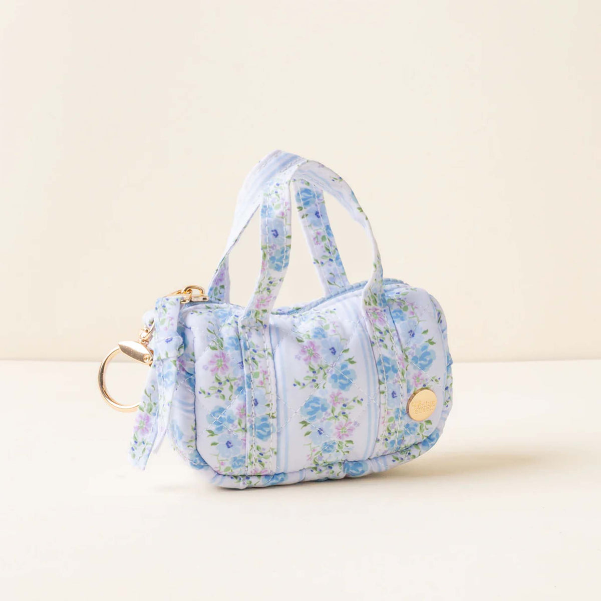 Side view of a pastel blue mini duffle keychain with blue and lavender floral print and gold keyring.