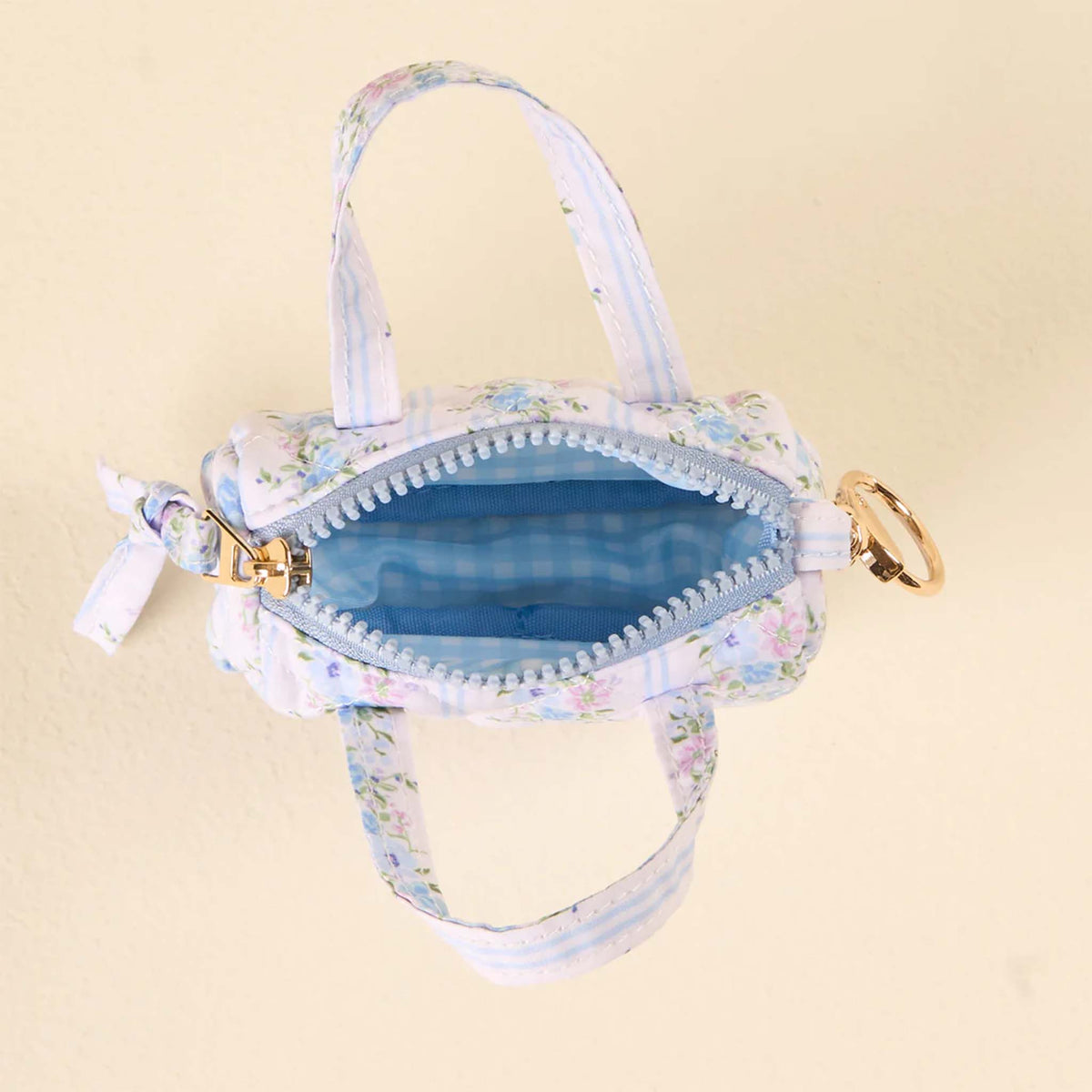 Top view of the mini floral keychain bag with zipper open, showing blue gingham interior lining.