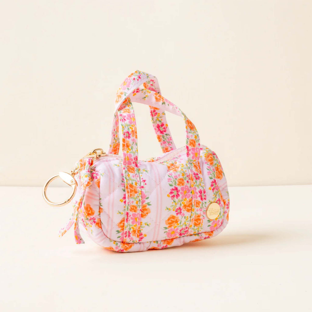 Side view of a pink quilted mini duffle keychain with floral stripe pattern and gold-tone keyring.