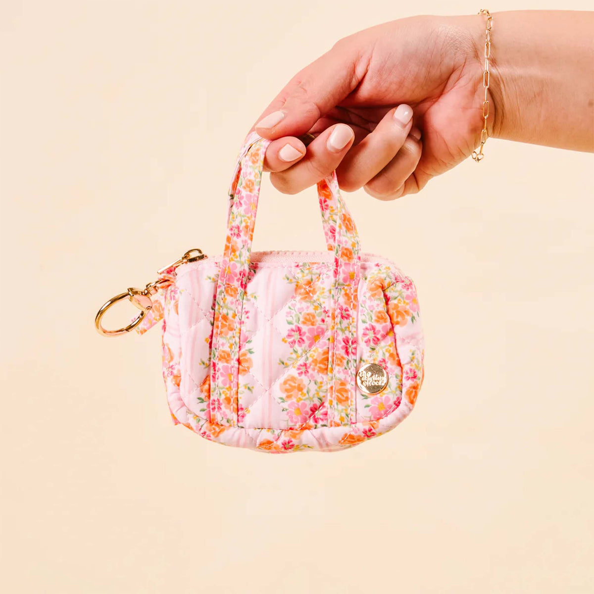 Hand holding pink floral mini duffle keychain, highlighting the floral design and gold logo charm.