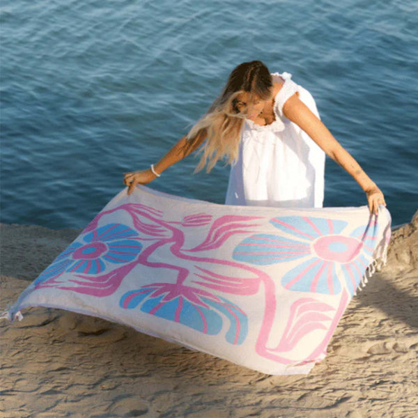Woman holding a colorful Sand Cloud towel with floral patterns on a beach.