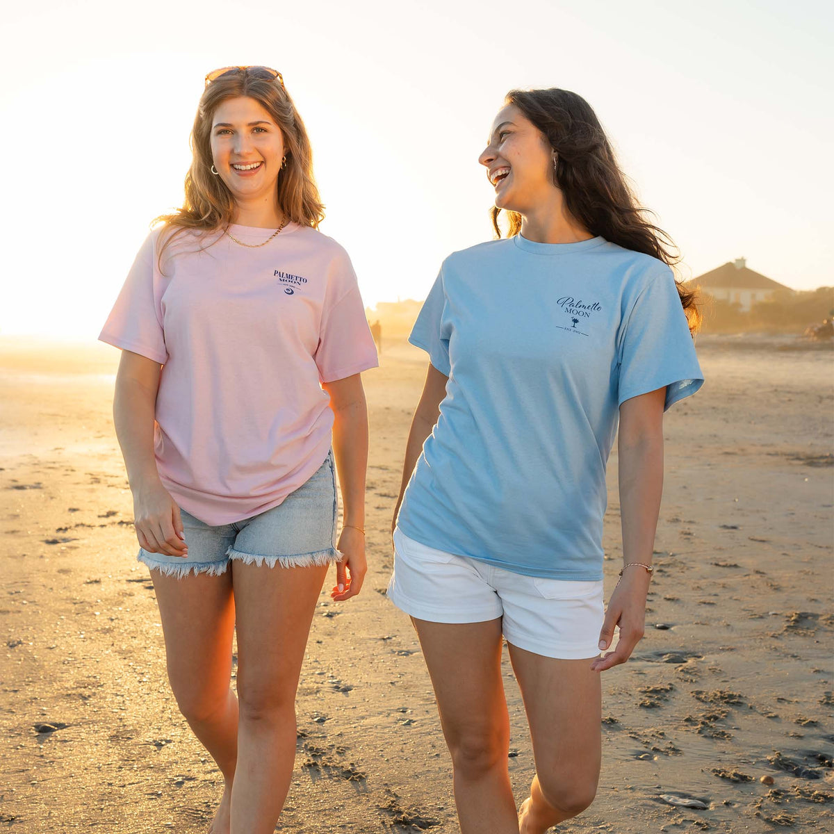 Two women walking on a beach wearing matching t-shirts.