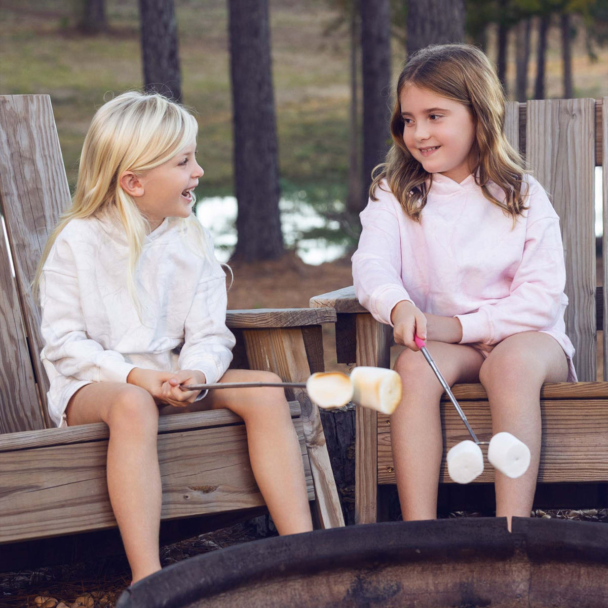 Two young girls roasting marshmallows over a campfire in a natural setting.