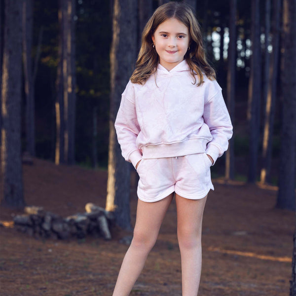 Young girl in a pink hoodie and shorts standing in a forest