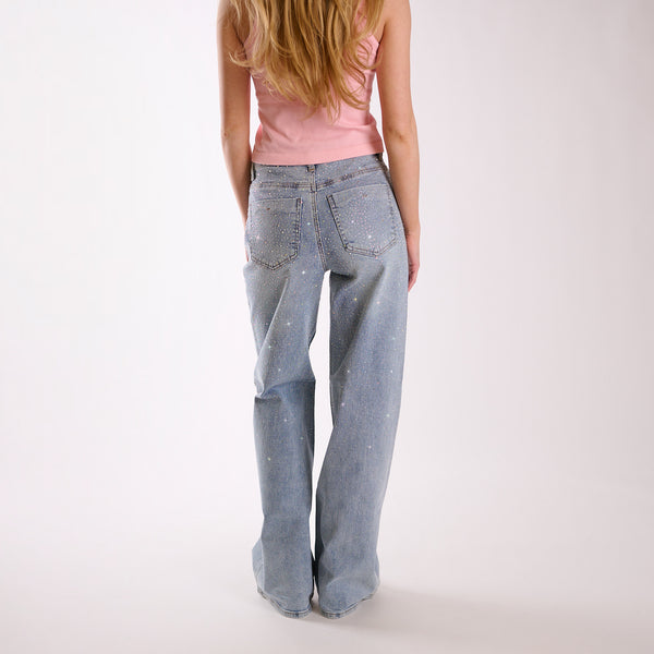 Woman wearing light blue flared jeans embellished with rhinestones and a pink top on a white background