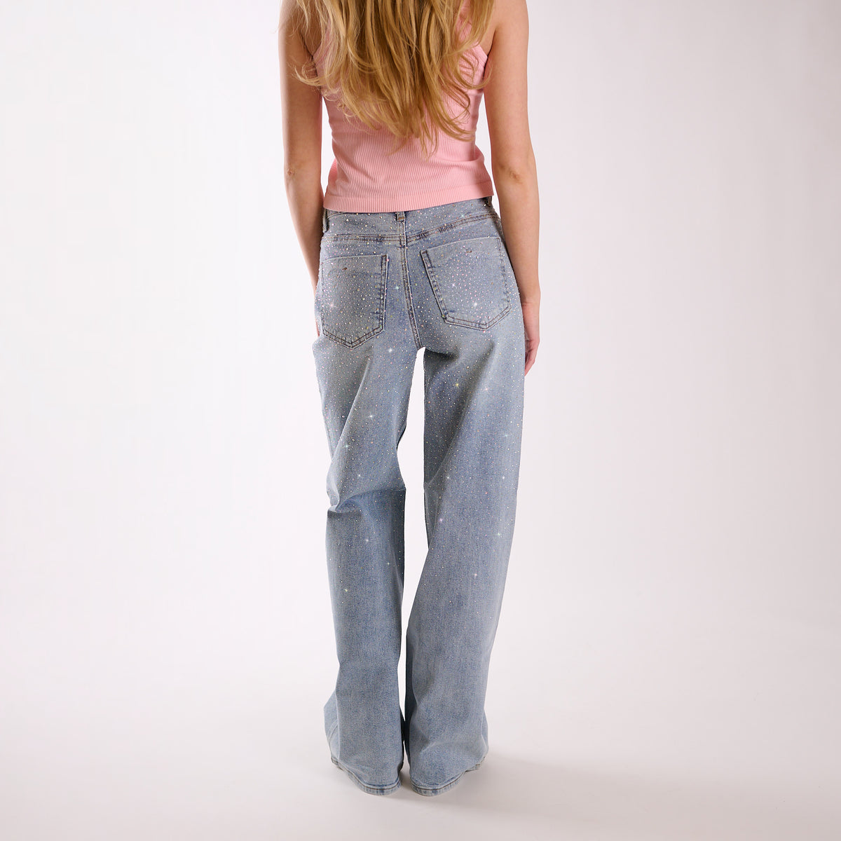 Woman wearing light blue flared jeans embellished with rhinestones and a pink top on a white background