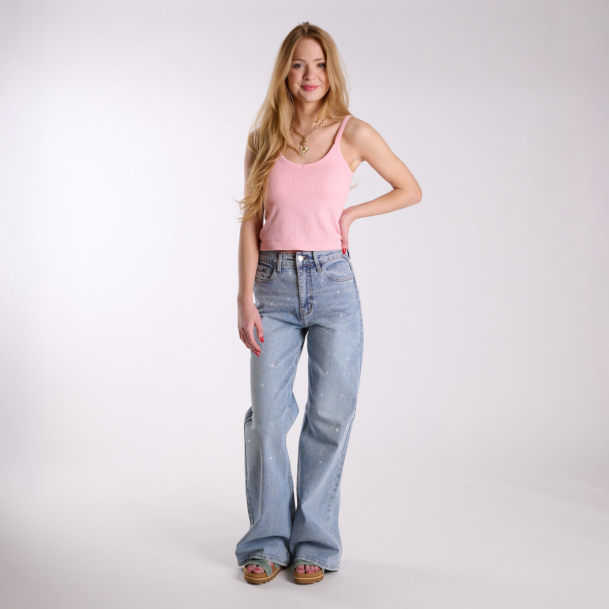 Woman wearing light blue flared jeans embellished with rhinestones and a pink top on a white background