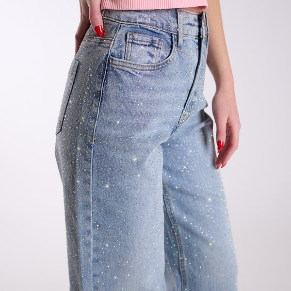 Close-up ofWoman wearing light blue flared jeans embellished with rhinestones and a pink top on a white background