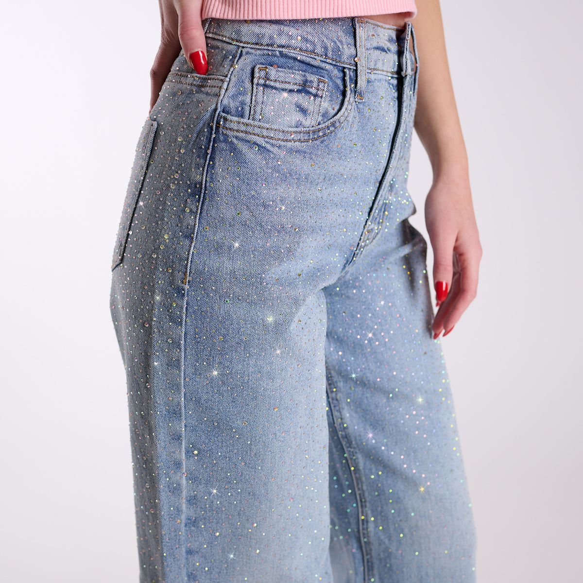 Close-up ofWoman wearing light blue flared jeans embellished with rhinestones and a pink top on a white background