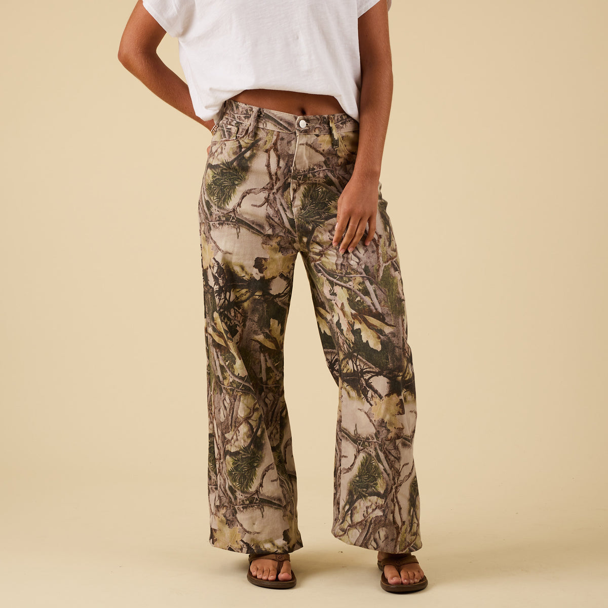 Front view of wide leg camo pants with button closure and relaxed silhouette, styled with white cropped tee.